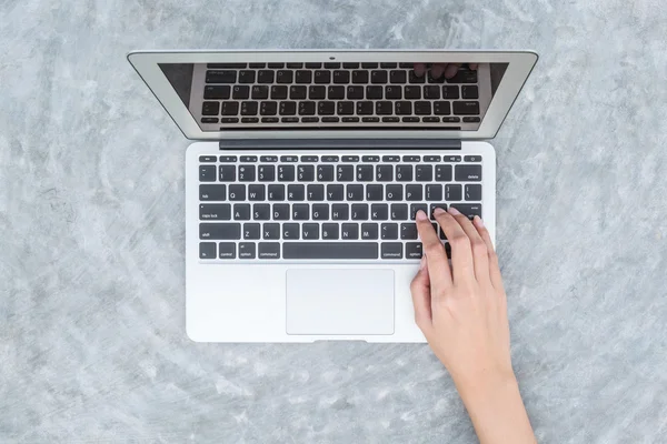 Primeros planos de la mujer escribiendo a mano en el teclado en el ordenador portátil gris en el escritorio de hormigón fondo texturizado en el jardín, el trabajo en el concepto al aire libre — Foto de Stock