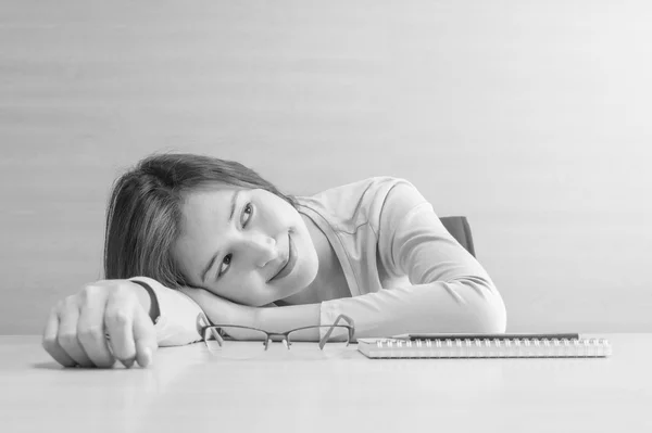 Closeup asian woman lied on desk with happy face in rest time from reading book on blurred wooden desk and wall textured background , happy time and relaxation of woman concept in black and white tone