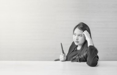 Toplantı odasında bulanık ahşap masa ve duvar dokulu arka plan üzerinde düşünme yüzü ve elinde bir kalem ile çalışan Closeup asya kadın , siyah ve beyaz tonda düşünme kavramı ile kadın