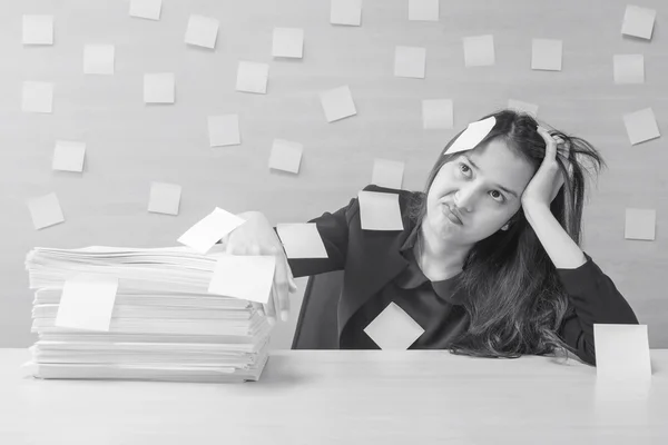 Closeup working woman are boring from hard work and pile of work paper in front of her in work concept on blurred wooden desk and wooden wall textured background in office room in black and white tone