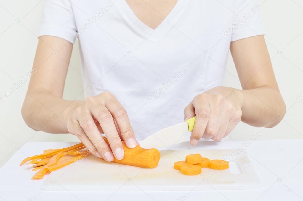 Closeup asian woman prepare for cooking with fresh carrot by plastic knife in her hand on old white plastic cutting board in the kitchen