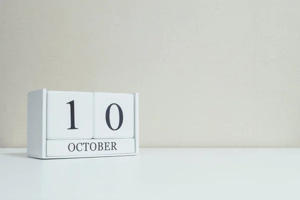 Nahaufnahme weißen Holzkalender mit schwarzen 10 Oktober Wort auf verschwommenem weißem Holz Schreibtisch und cremefarbene Tapete im Raum strukturierten Hintergrund mit Kopierraum, sehen Sie ein weiteres Datum in meinem Portfolio — Stockfoto