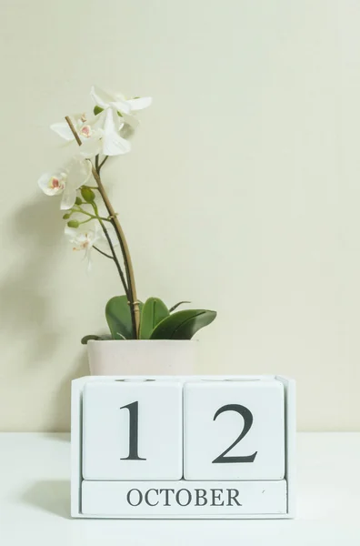 Gros plan calendrier en bois blanc avec noir 12 mot d'octobre avec fleur d'orchidée blanche sur bureau en bois blanc et papier peint de couleur crème dans la chambre fond texturé, voir une autre date dans mon portefeuille — Photo