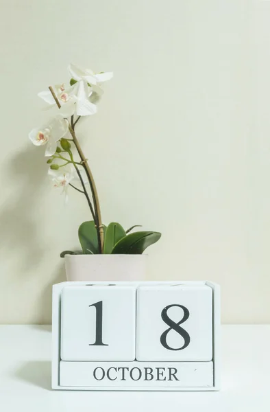 Gros plan calendrier en bois blanc avec mot noir 18 octobre avec fleur d'orchidée blanche sur bureau en bois blanc et papier peint de couleur crème dans la chambre fond texturé, voir une autre date dans mon portefeuille — Photo