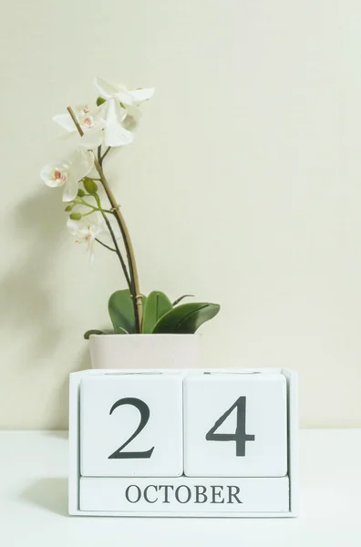 Closeup calendário de madeira branca com preto 24 palavra de outubro com flor de orquídea branca na mesa de madeira branca e papel de parede cor creme no quarto fundo texturizado, foco seletivo no calendário — Fotografia de Stock