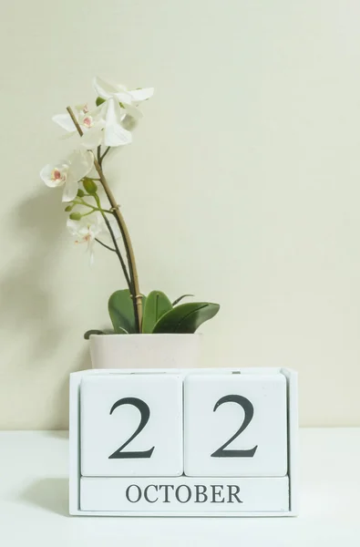 Gros plan calendrier en bois blanc avec noir 22 mot d'octobre avec fleur d'orchidée blanche sur bureau en bois blanc et papier peint de couleur crème dans la chambre fond texturé, mise au point sélective au calendrier — Photo