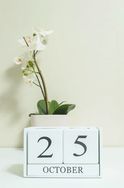 Closeup calendário de madeira branco com preto 25 palavra de outubro com flor de orquídea branca na mesa de madeira branca e papel de parede cor creme no quarto fundo texturizado, foco seletivo no calendário — Fotografia de Stock