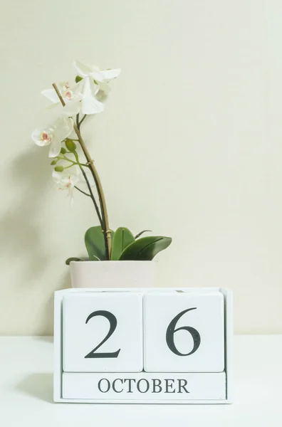 Closeup calendário de madeira branco com preto 26 palavra de outubro com flor de orquídea branca na mesa de madeira branca e papel de parede cor creme no quarto fundo texturizado, foco seletivo no calendário — Fotografia de Stock
