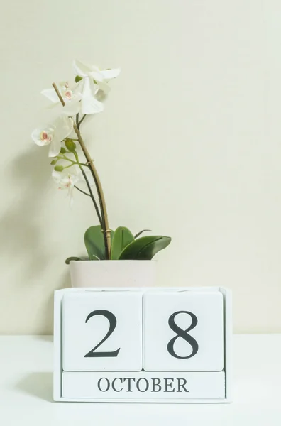 Closeup calendário de madeira branco com preto 28 palavra de outubro com flor de orquídea branca na mesa de madeira branca e papel de parede cor creme no quarto fundo texturizado, foco seletivo no calendário — Fotografia de Stock