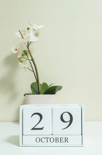 Closeup calendário de madeira branca com preto 29 palavra de outubro com flor de orquídea branca na mesa de madeira branca e papel de parede cor creme no quarto fundo texturizado, foco seletivo no calendário — Fotografia de Stock