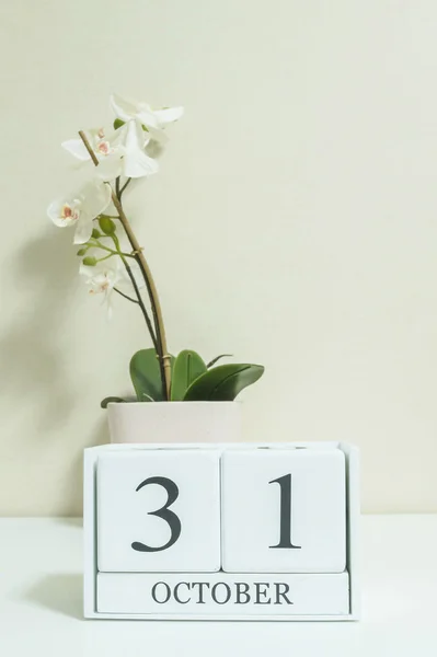 Closeup calendário de madeira branco com preto 31 palavra de outubro com flor de orquídea branca na mesa de madeira branca e papel de parede cor creme no quarto fundo texturizado, foco seletivo no calendário — Fotografia de Stock