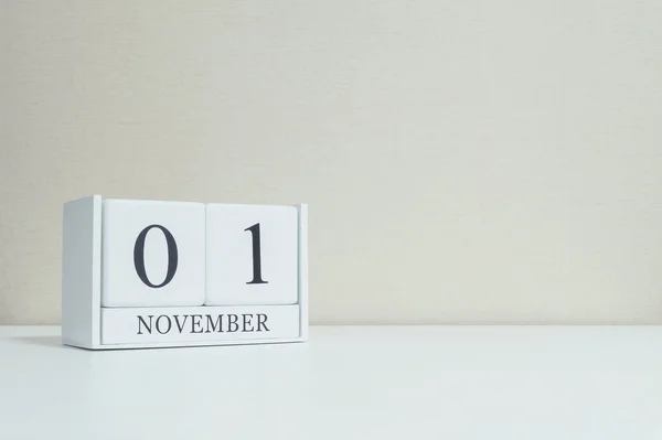 Крупный план белый деревянный календарь с черным 1 ноября слово на размытый стол белого дерева и кремовый цвет обоев в комнате текстурированный фон с копировальным пространством, избирательный фокус на календаре — стоковое фото