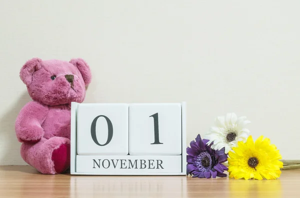 Surface rapprochée calendrier en bois blanc avec noir 1 novembre mot sur bureau en bois brun et papier peint de couleur crème dans la chambre fond texturé avec espace de copie, mise au point sélective au calendrier — Photo