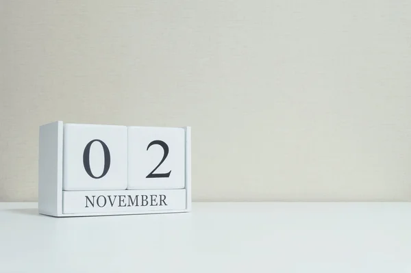 Nahaufnahme weißer Holzkalender mit schwarzem Wort vom 2. November auf verschwommenem weißem Holztisch und cremefarbener Tapete im Raum strukturierten Hintergrund mit Kopierraum, selektiver Fokus auf den Kalender — Stockfoto