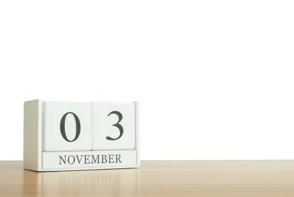 Nahaufnahme Oberfläche weißer Holzkalender mit schwarzem Wort vom 3. November auf unscharfem braunem Holztisch isoliert auf weißem Hintergrund mit Kopierraum, selektiver Fokus auf den Kalender — Stockfoto