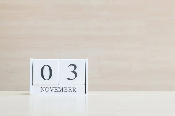 Nahaufnahme Oberfläche weißer Holzkalender mit schwarzem Wort vom 3. November auf unscharfem braunem Holz-Schreibtisch und Holz-Wand strukturiertem Hintergrund mit Kopierraum, selektiver Fokus auf den Kalender — Stockfoto