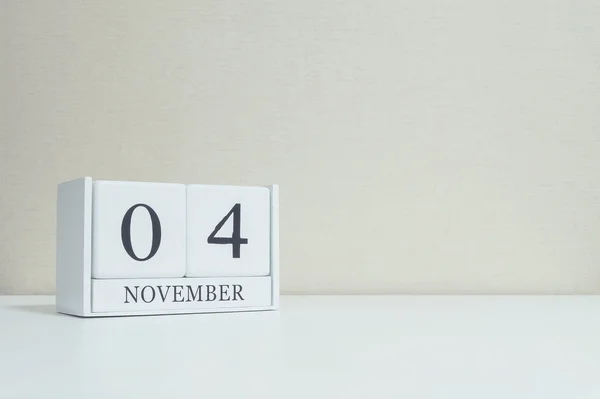 Nahaufnahme weißer Holzkalender mit schwarzem Wort vom 4. November auf verschwommenem weißem Holztisch und cremefarbener Tapete im Raum strukturierten Hintergrund mit Kopierraum, selektiver Fokus auf den Kalender — Stockfoto