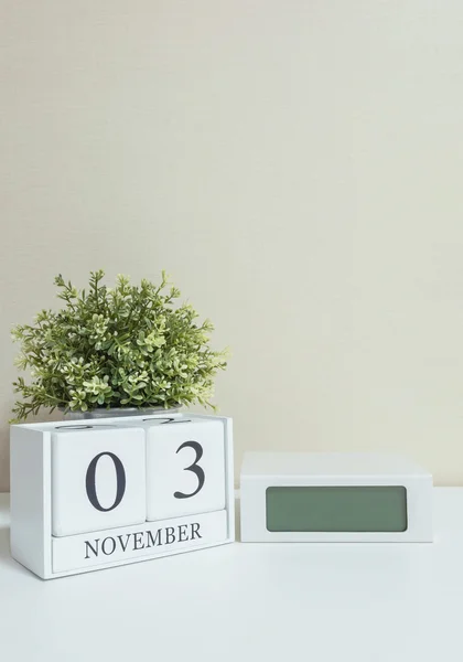 Calendario de madera blanca con negro 3 palabra de noviembre con reloj y planta sobre escritorio de madera blanca y fondo de pantalla crema textura, enfoque selectivo en el calendario — Foto de Stock