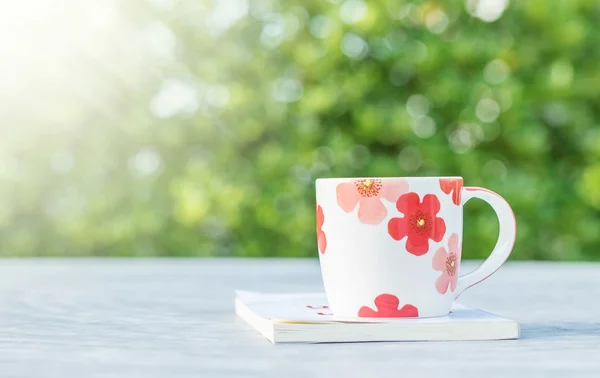 Nahaufnahme niedliche Tasse Kaffee weißes Buch auf verschwommenem Beton Schreibtisch und Blick auf den Garten am Morgen strukturierten Hintergrund — Stockfoto