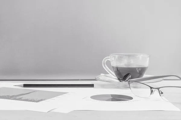 Closeup μαύρο καφέ στο φλιτζάνι του καφέ με εργασία χαρτί και μολύβι και γυαλιά on θολή επιφάνεια και γυάλινο τοίχο υφή φόντου, εργάζονται έννοια από καφέ και εργάζονται χαρτί σε μαύρο και άσπρο τόνος — Φωτογραφία Αρχείου