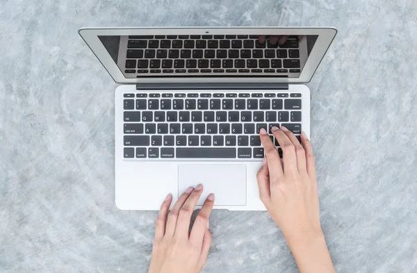 Primeros planos mujer escribiendo a mano en el teclado en el ordenador portátil gris en el escritorio de hormigón fondo texturizado bajo la luz del día en el jardín en la vista superior — Foto de Stock