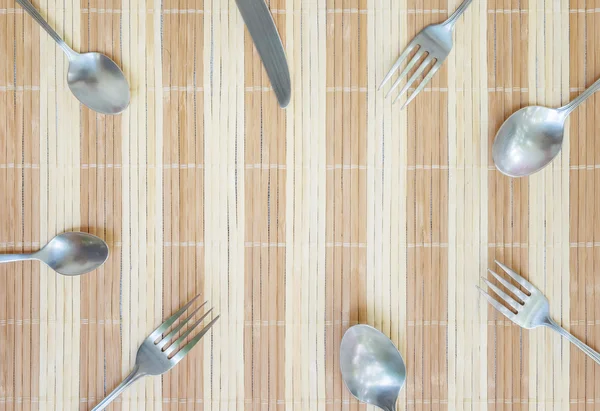 Närbild-gruppen av rostfritt stål gaffel sked och kniv på trä matta texturerat bakgrund med kopia utrymme vid center i ovanifrån — Stockfoto