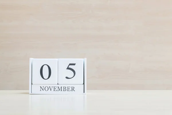 Nahaufnahme Oberfläche weißer Holzkalender mit schwarzem Wort vom 5. November auf unscharfem braunem Holz-Schreibtisch und Holz-Wand strukturiertem Hintergrund mit Kopierraum, selektiver Fokus auf den Kalender — Stockfoto