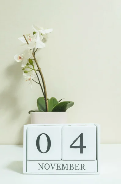 Gros plan calendrier en bois blanc avec mot noir 4 novembre avec fleur d'orchidée blanche sur bureau en bois blanc et papier peint de couleur crème dans la chambre fond texturé, mise au point sélective au calendrier — Photo