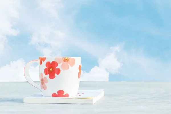 Closeup cute cup of coffee white book on blurred concrete desk in the garden with beautiful blue sky with cloud in the morning textured background