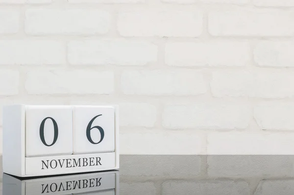 Ξύλινο ημερολόγιο closeup λευκό με μαύρο 6 Νοεμβρίου λέξη σε μαύρο γυαλί τούβλο πίνακας και το λευκό τοίχο φόντο με υφή με το διάστημα αντίγραφο, επιλεκτική εστίαση στο ημερολόγιο — Φωτογραφία Αρχείου