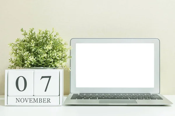 Άσπρο ξύλινες ημερολόγιο με μαύρο 7 Νοεμβρίου λέξη με λευκό κενό χώρο στο κέντρο του υπολογιστή notebook σε λευκό ξύλινο γραφείο και κρέμα ταπετσαρία υφή φόντου, επιλεκτική εστίαση στο ημερολόγιο — Φωτογραφία Αρχείου