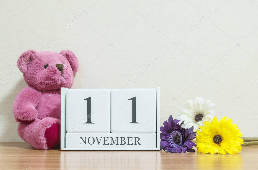 Closeup surface white wooden calendar with black 11 november word on brown wood desk and cream color wallpaper in room textured background with copy space , selective focus at the calendar