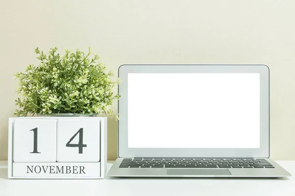 Білий дерев'яний календар з чорним 14 листопада слово з білим порожнім простором в центрі комп'ютерного ноутбука на білому дерев'яному столі і кремових шпалерах текстурованого фону, вибірковий фокус на календарі — стокове фото