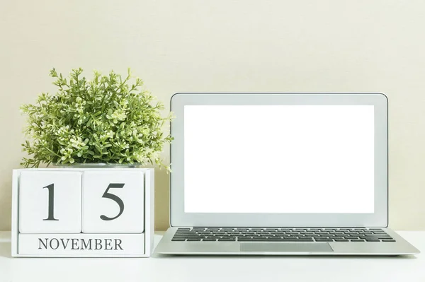 Άσπρο ξύλινες ημερολόγιο με μαύρο λέξη 15 Νοεμβρίου με λευκό κενό χώρο στο κέντρο του υπολογιστή notebook σε λευκό ξύλινο γραφείο και κρέμα ταπετσαρία υφή φόντου, επιλεκτική εστίαση στο ημερολόγιο — Φωτογραφία Αρχείου