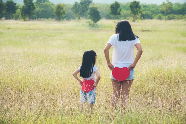 Mãe e filha de pé segurando um coração vermelho suas costas — Fotografia de Stock