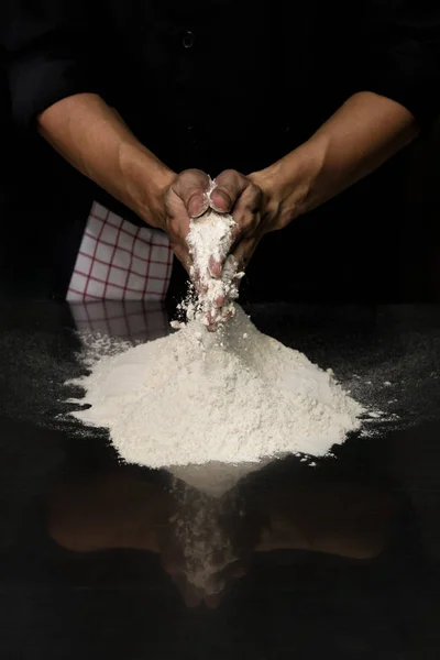 hands chef black cloth knead white flour dough on a table