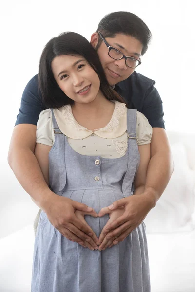Cheerful adult asian couple with pregnancy on white at home