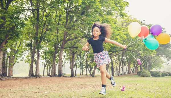 Dítě dívka běží na jarním poli ve veřejném parku s balónem — Stock fotografie