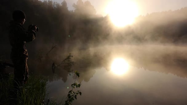 Egy férfi fényképezi a reggeli ködöt. Meleg nyári táj — Stock videók