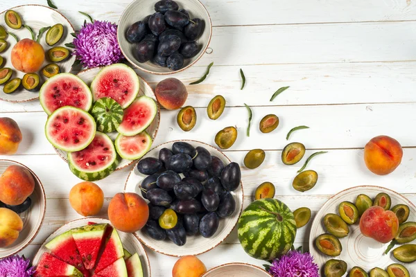 Colorful fruit set of purple, red and orange background in bowls. Plum, peaches, watermelon sliced above white tabletop