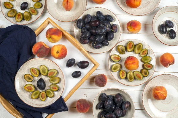 Colorful fruit set of purple, red and orange background in bowls. Plum, peaches, watermelon sliced above white tabletop