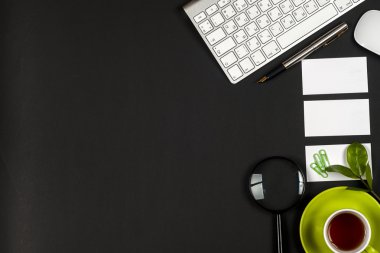 Ofis siyah resepsiyon masası beyaz bilgisayar, boş kartvizit, çiçek, kahve fincanı ve kalem.