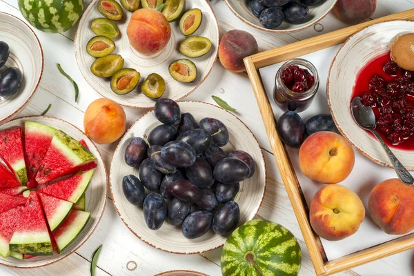 Conjunto de frutas coloridas de fundo roxo, vermelho e laranja em tigelas. Ameixa, pêssegos, melancia fatiada acima da mesa branca — Fotografia de Stock