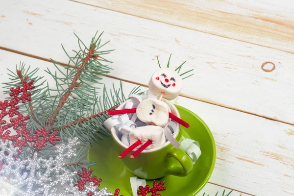 Christmas card with fun marshmallow snowman in green cup, tree — Stock Photo, Image