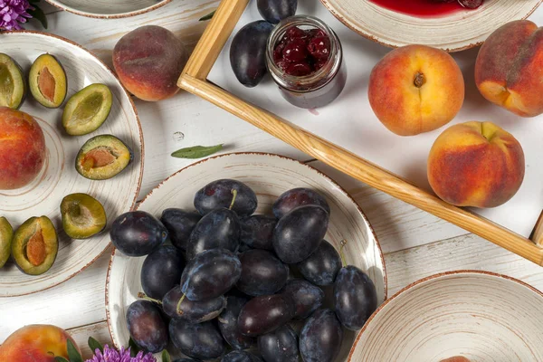 Colorful fruit set of purple, red and orange background in bowls. Plum, peaches, watermelon sliced above white tabletop