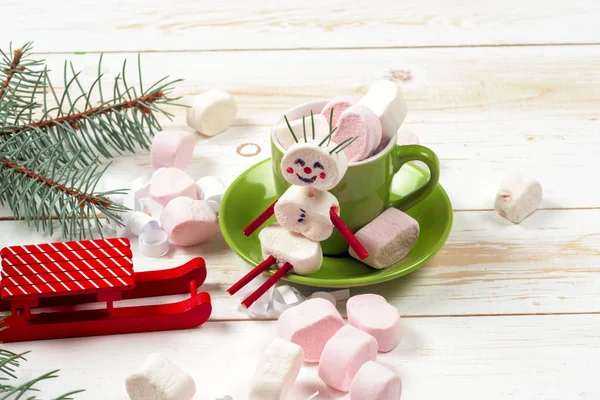 Weihnachtskarte mit lustigem Marshmallow-Schneemann in grüner Tasse, Baum — Stockfoto