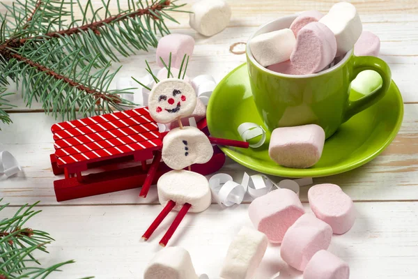 Christmas card with fun marshmallow snowman in green cup, tree — Stock Photo, Image