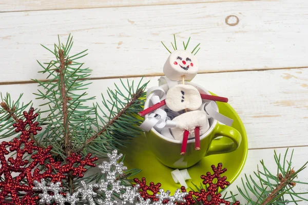 Christmas card with fun marshmallow snowman in green cup, tree — Stock Photo, Image