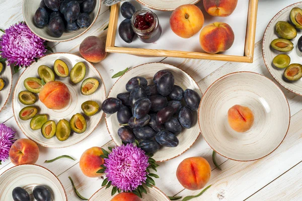 Colorful fruit set of purple, red and orange background in bowls. Plum, peaches, watermelon sliced above white tabletop