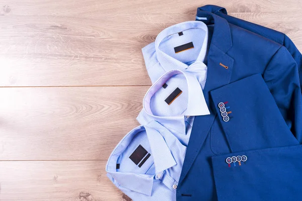 Düz ahşap zemin üzerine mavi takım elbise, gömlek, kahverengi ayakkabı, kemer ve kravat gibi klasik erkek giysi set koymak.